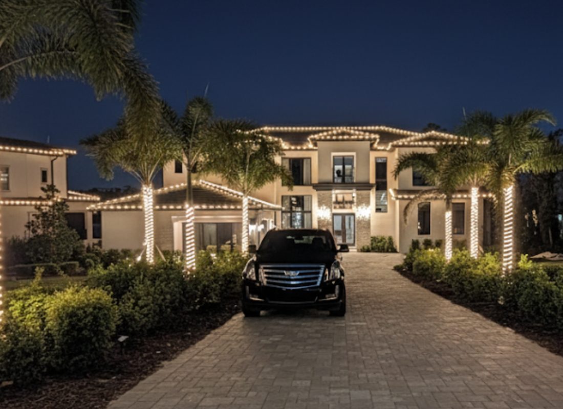Estate with warm white roofline lights and wrapped palm trees